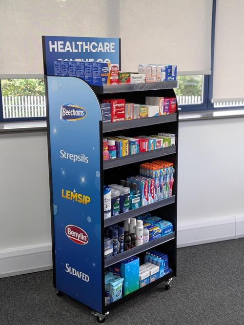 Healthcare on the go point-of-sale display stand with a printed blue side panel, stocked with cold, flu and toiletry products