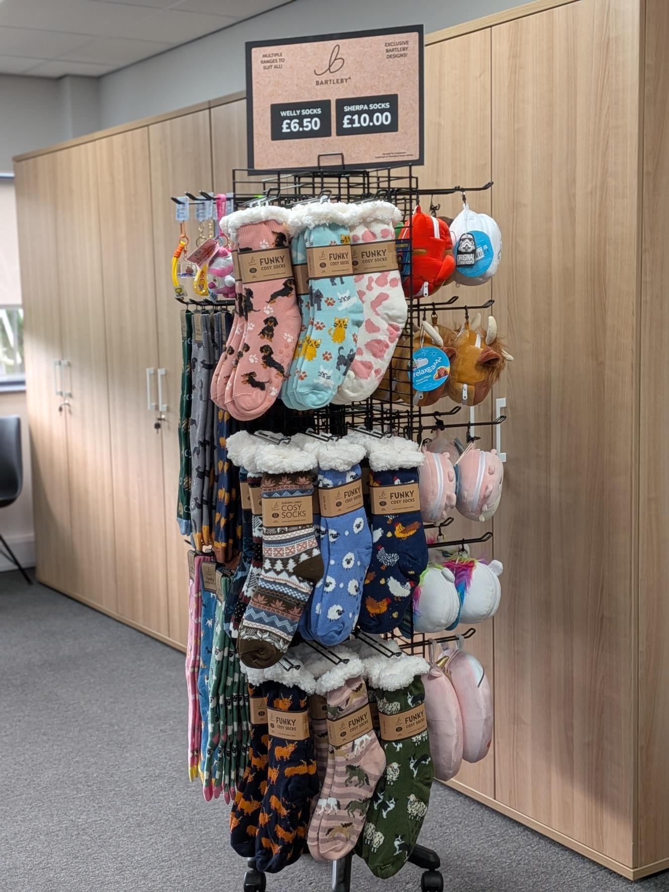 Rotating retail display of Bartleby cosy socks and plush travel pillows with a printed price header card