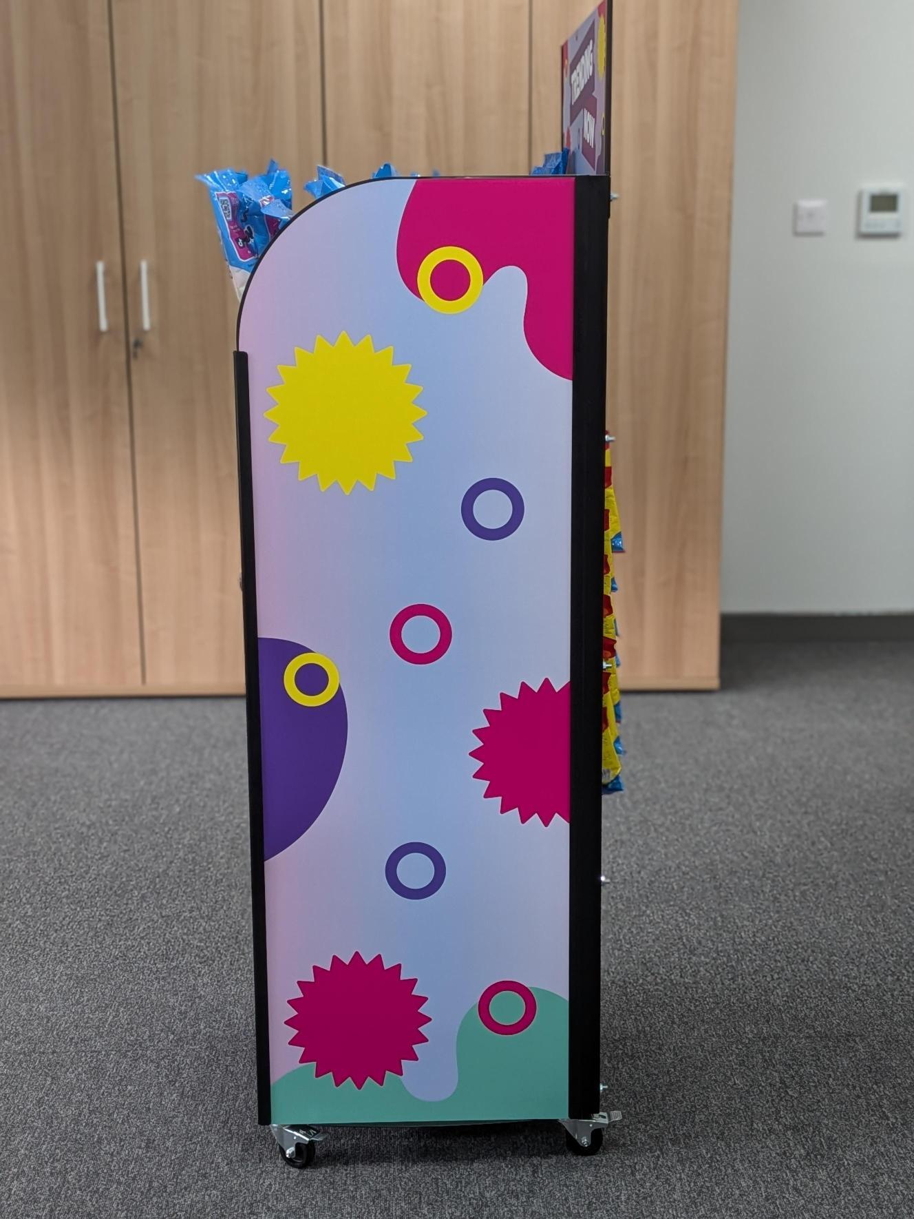 Side panel of a mobile retail display unit printed with bold pink, purple and yellow graphics